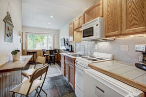 A kitchen with wooden cabinets, a microwave, a stove, and a dining area with chairs and a table.