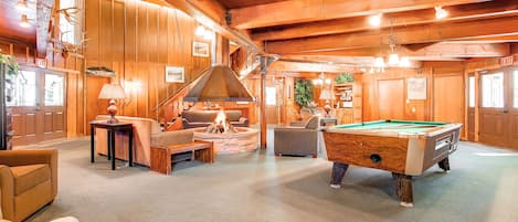 Ein gemütliches Lodge-Interieur mit Billardtisch, bequemen Sitzgelegenheiten, Kamin und Holzwänden.