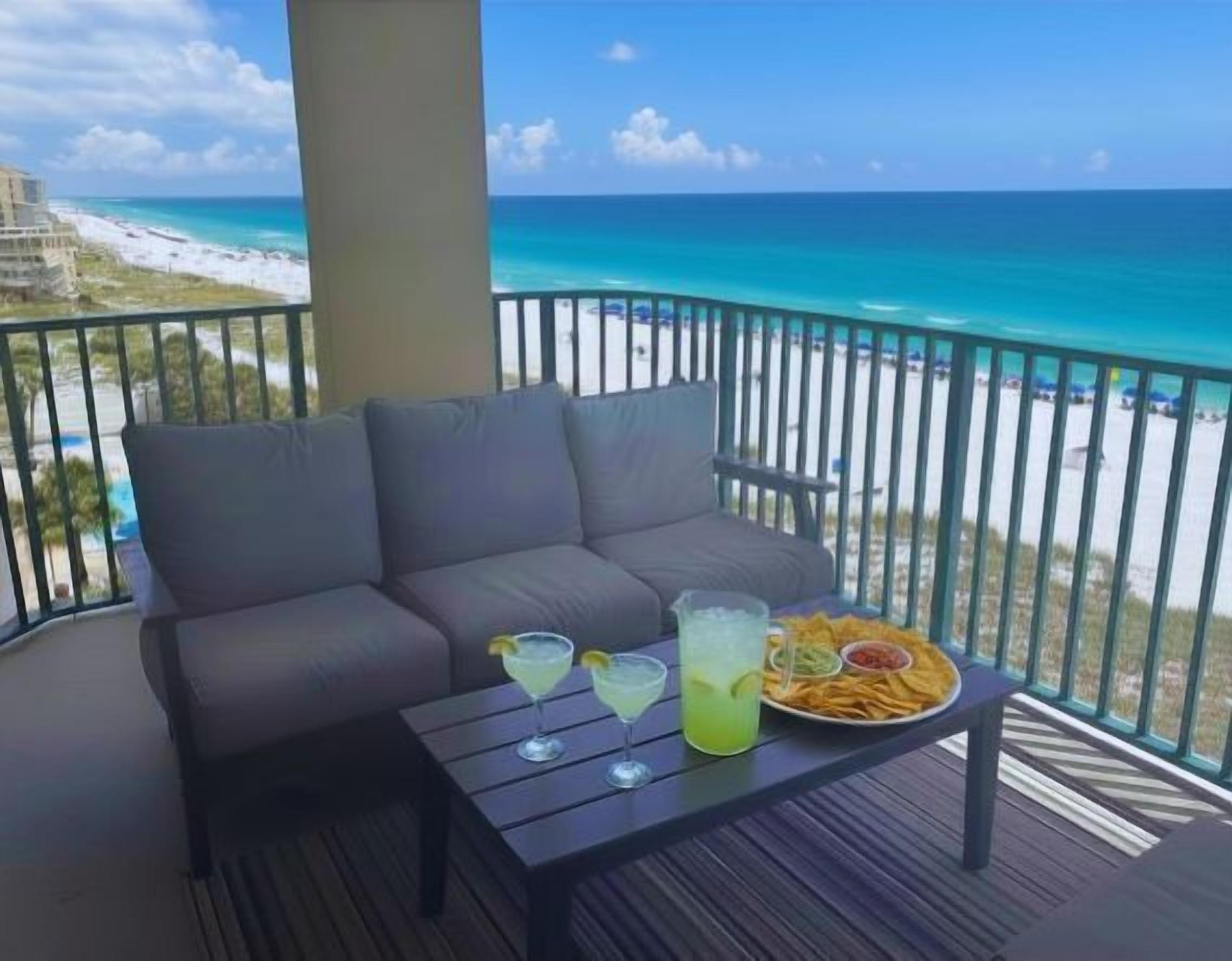 A balcony with a sofa and table, a drink, and a plate of food.