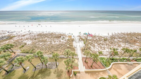 A beach resort with a boardwalk leading to a beach area, a lifeguard tower, and a flagpole with flags.