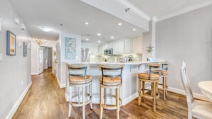 A modern kitchen with white cabinets, a central island with bar stools, and a starfish decoration on the wall. - Stunning Gulf Views I Luxury Beachfront I Jade East Towers 620 (Destin)