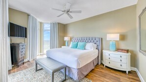 A hotel room with a bed, a bench, a nightstand, a TV, and a ceiling fan. - Stunning Gulf Views I Luxury Beachfront I Jade East Towers 620 (Destin)