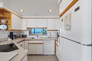A kitchen with white cabinets, a dishwasher, a coffee maker, and a window with a view.