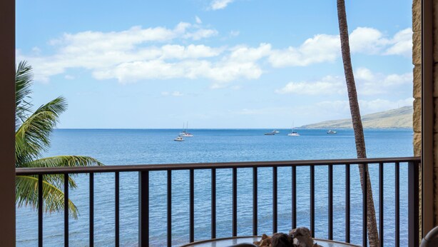Ein Balkon mit Blick auf das Meer, Palmen und einem Tisch mit einer Obstschale.