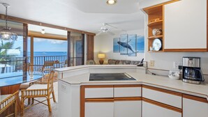Eine moderne Küche mit einer zentralen Kochinsel, einem Essbereich mit Korbstühlen, einer Kaffeemaschine und Meerblick.