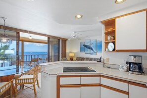 Een moderne keuken met een centraal eiland, een eethoek met rieten stoelen, een koffiezetapparaat en uitzicht op de oceaan.