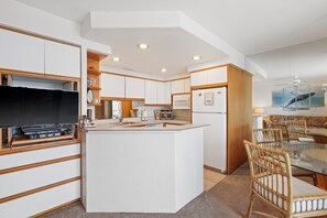 Een moderne keuken met een centraal eiland, houten keukenkastjes, en een eethoek met een glazen tafel en rieten stoelen.