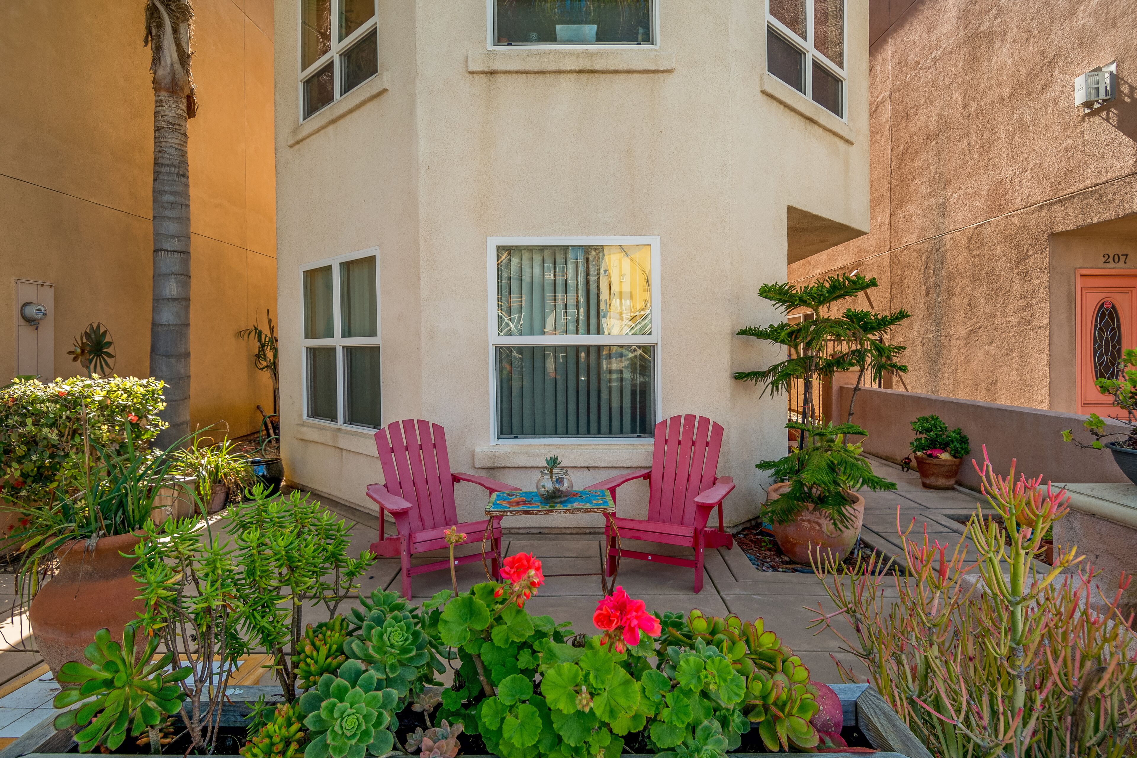 A patio with two pink chairs, a table, and various potted plants.
