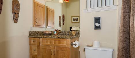 A bathroom with wooden cabinets, a granite countertop, a toilet, a mirror, and a sun-shaped light fixture.
