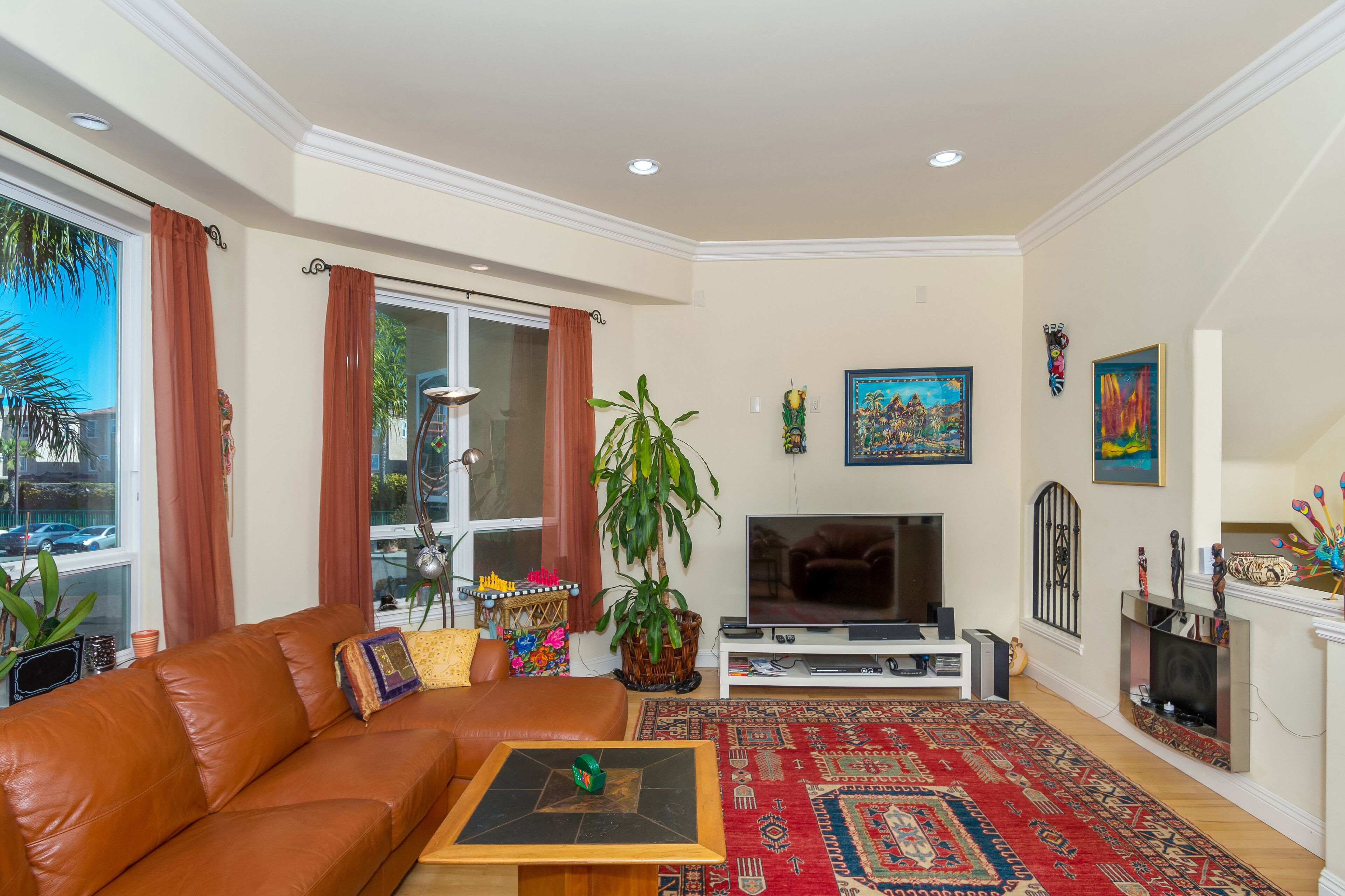 A living room with a brown leather sofa, a wooden coffee table, a TV, a fireplace, and a red patterned rug.