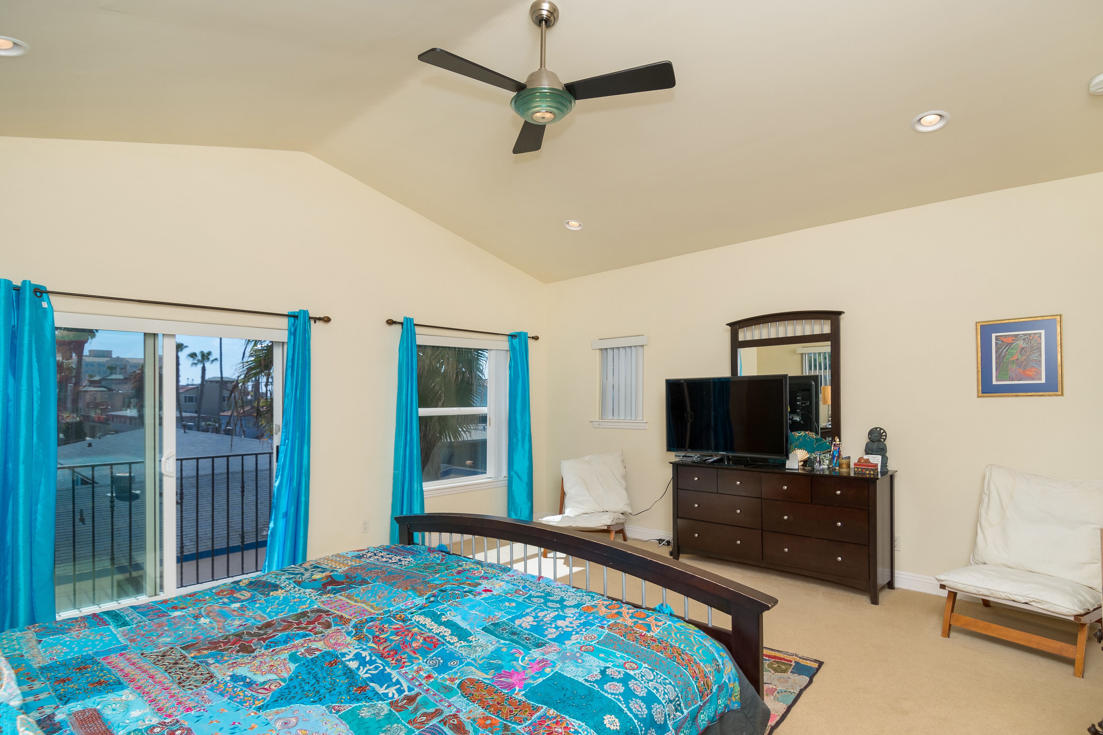 A bedroom with a bed, a dresser, a chair, a TV, and a ceiling fan.