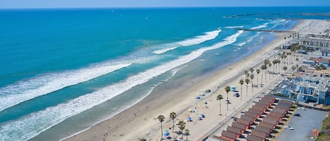 A beachside hotel with multiple rooms, a sandy beach, and a view of the ocean.