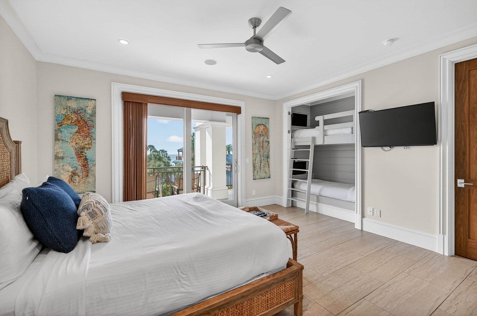 A bedroom with a bed, a ceiling fan, a TV, and a balcony with a view.