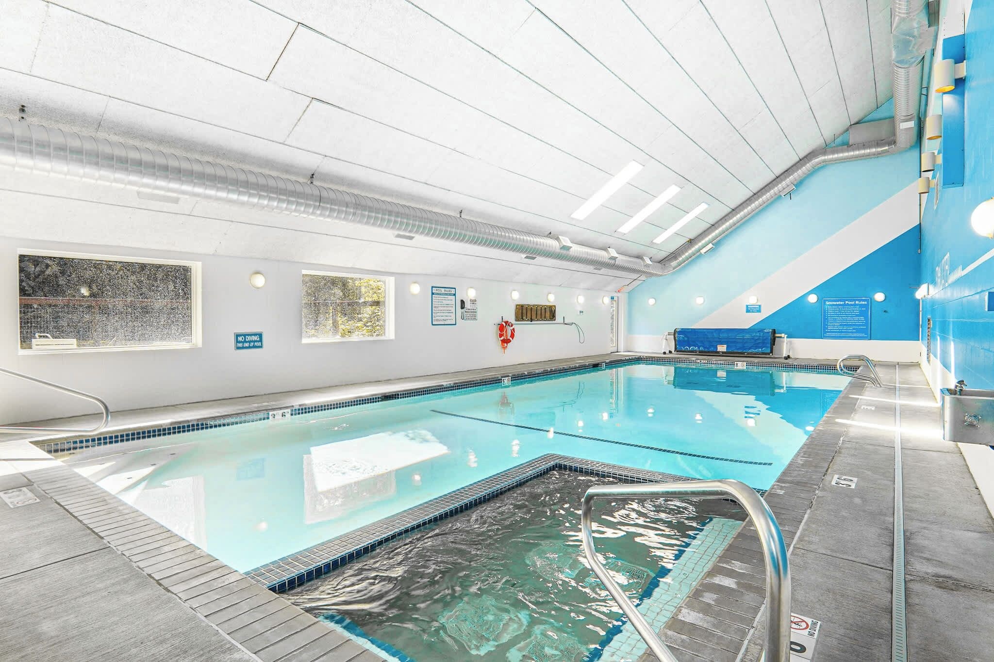 An indoor swimming pool with clear water, a diving board, and safety equipment.