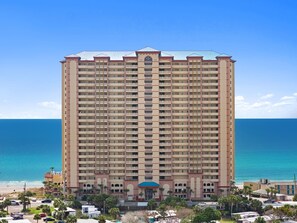 Un hotel de gran altura con múltiples balcones, una entrada central y vistas al océano.