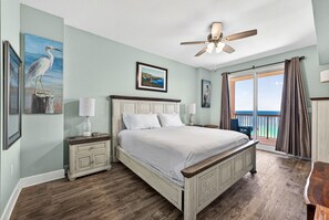 Un dormitorio con cama, mesita de noche, lámpara, ventilador de techo y vistas al exterior.