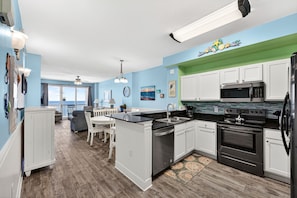 A kitchen with white cabinets, a black countertop, stainless steel appliances, and a view to the outside.