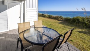 A glass-top table with four chairs on a wooden deck, overlooking a grassy area and the ocean. - Gulf front townhouse with community pool, incredible views- Blue Mountain Beach (Santa Rosa Beach)