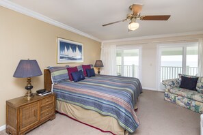 A bedroom with a large bed, two bedside tables, a ceiling fan, and a view of the outdoors through a window.