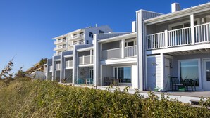 A coastal residential building with multiple balconies, large windows, and a grassy foreground. - Gulf front townhouse with community pool, incredible views- Blue Mountain Beach (Santa Rosa Beach)