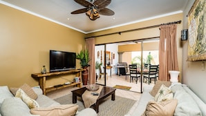 A living room with a TV, sofa, coffee table, and a ceiling fan. - Sunrise 30, beautiful Condo In the Heart of Town (Tamarindo)