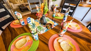 A round wooden dining table with colorful tropical-themed tableware and a centerpiece. - Sunrise 30, beautiful Condo In the Heart of Town (Tamarindo)