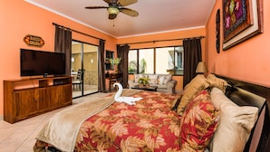 A hotel room with a bed, a television, a ceiling fan, a sofa, and a view of the outdoors. - Sunrise 30, beautiful Condo In the Heart of Town (Tamarindo)
