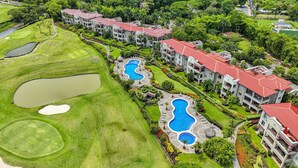 En golfbane med flere vandhuller og et swimmingpoolområde ved siden af et resort med røde tage.