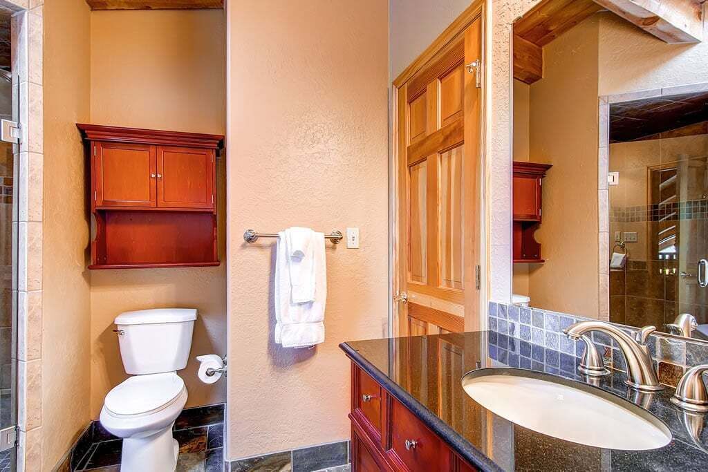 A bathroom with a toilet, wooden cabinets, a sink with a mirror, and a towel hanging on the wall.