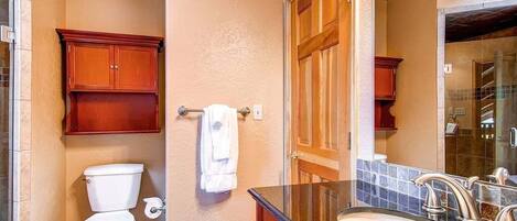 A bathroom with a toilet, wooden cabinets, a sink with a mirror, and a towel hanging on the wall.
