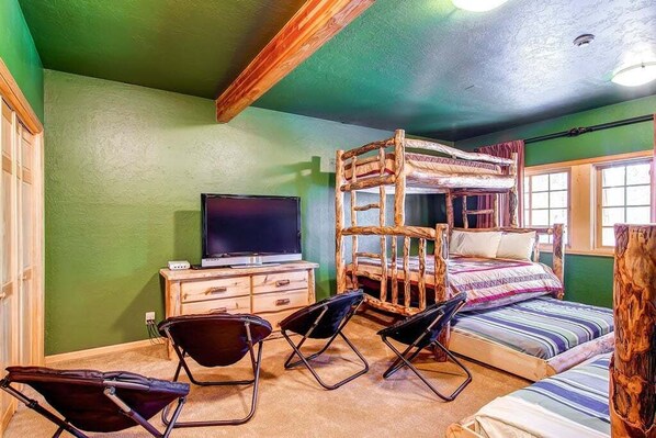 Un lit superposé avec un téléviseur posé sur une commode, un bureau et deux chaises dans une pièce aux murs verts.