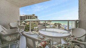 Un balcon agrémenté de meubles en osier et d’une table en verre, offrant une vue sur la plage et les bâtiments de l’hôtel.