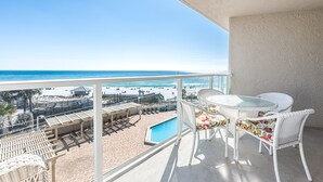 Un balcon avec vue sur la plage, une piscine et un espace salon extérieur.