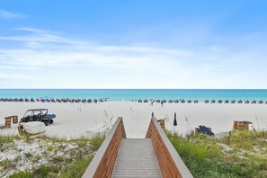 Ein hölzerner Steg führt zu einem Strand unter blauem Himmel.