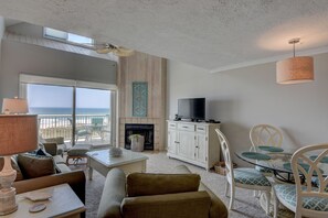 Relax in a spacious living room with a sofa, armchairs, and fireplace, offering a view of the ocean through large glass doors.