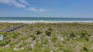 Un paysage côtier avec une promenade en bois menant à la plage, le tout entouré d’une zone herbeuse.