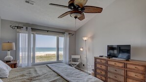 Une chambre avec un lit, une télévision, une commode et une vue sur la plage.