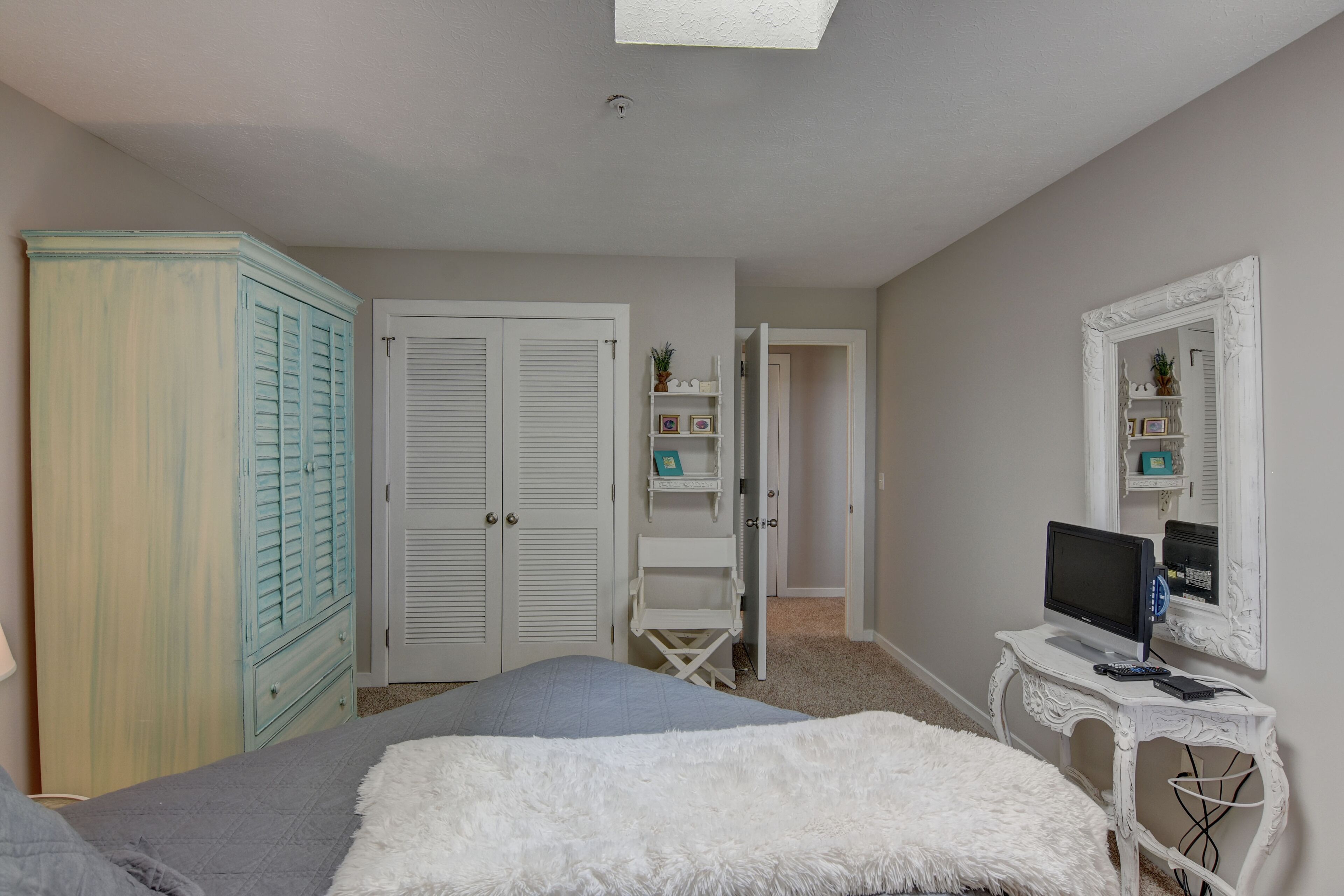 A bedroom with a bed, a wardrobe, a desk with a computer, and a mirror.