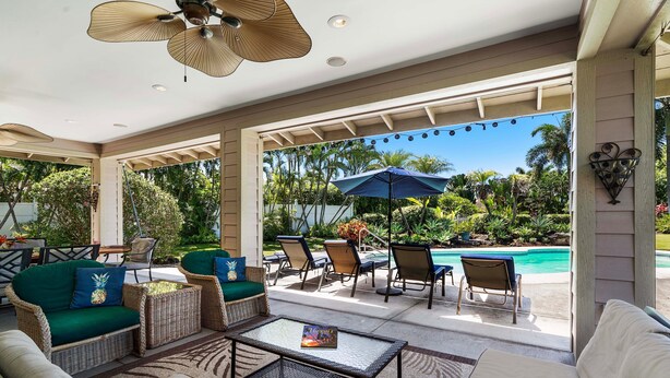 Un espace extérieur aménagé, abrité et doté de mobilier en osier, d’une table en verre et offrant une vue sur une piscine.