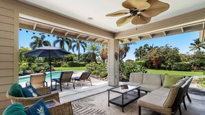 Un patio couvert aménagé avec du mobilier d’extérieur, un ventilateur de plafond et une vue sur une piscine et un paysage tropical.