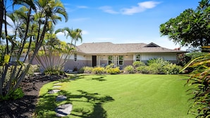Une maison dotée d’une pelouse bien entretenue, d’un chemin en pierre et de plantes tropicales.
