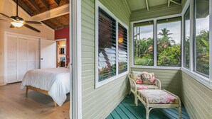 Un dormitorio con cama, ventilador de techo y vistas a un jardín exuberante a través de amplias ventanas.