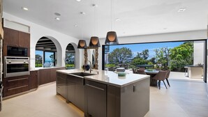 Une cuisine moderne dotée d’un îlot central, d’appareils électroménagers intégrés et offrant une vue sur l’extérieur.