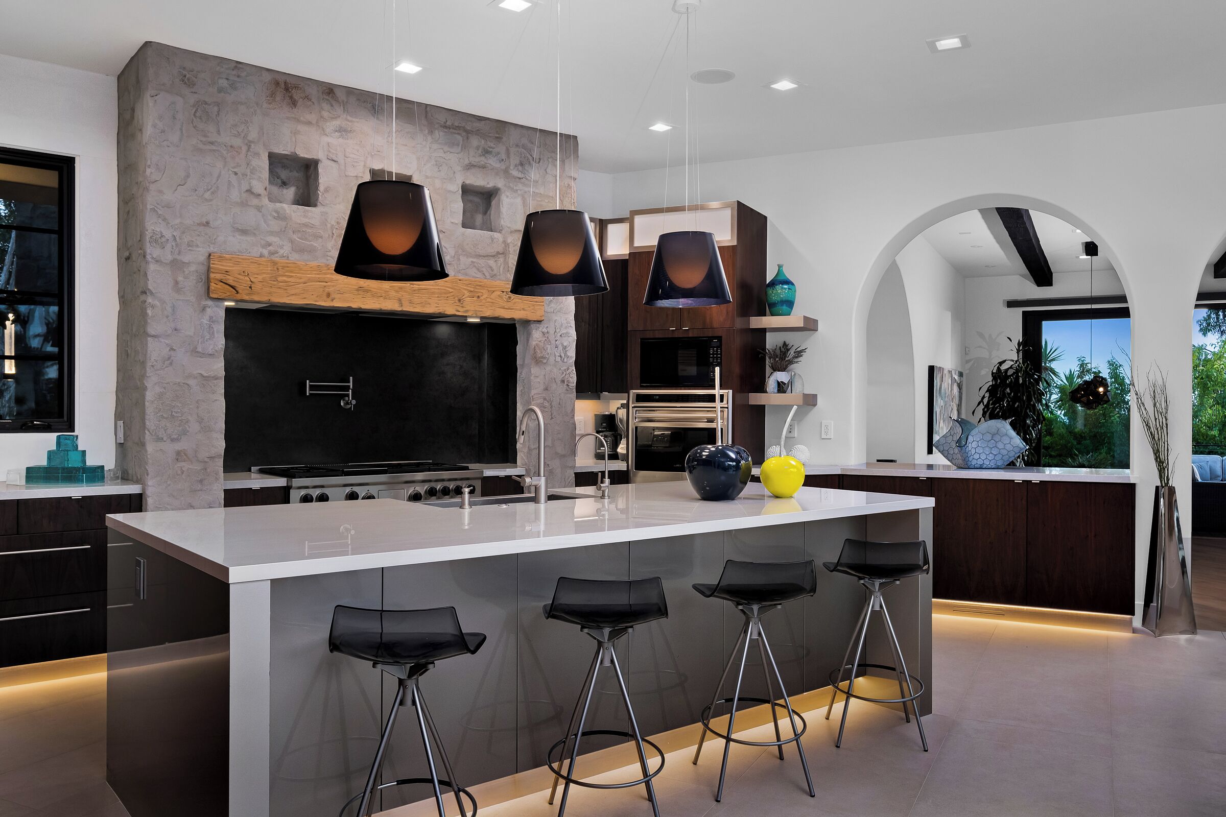 Una cocina moderna con una isla central, taburetes de bar y una pared de acento de piedra.