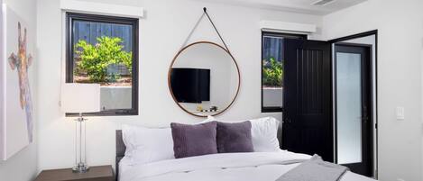 Een moderne slaapkamer met een bed, nachtkastje, lamp en een aan de muur bevestigde televisie.