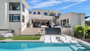 Une maison moderne à deux étages, dotée d’une piscine, d’un espace de détente extérieur et d’un escalier menant à l’étage supérieur.