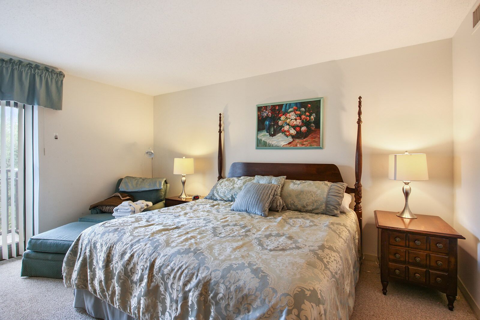 Une chambre à coucher avec un lit à baldaquin, une table de chevet avec une lampe, une chaise et un tableau accroché au mur.