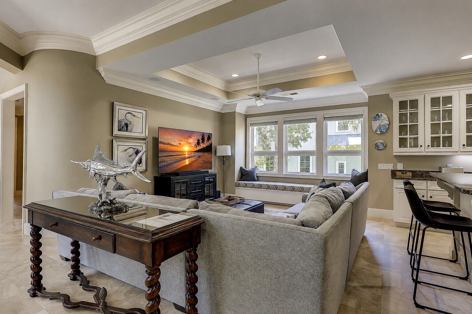 A spacious living room with a large sofa, a wooden coffee table, and a television. There is a dining area with a kitchen counter and cabinets.