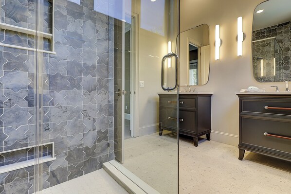 A bathroom with a glass shower enclosure, a dark vanity with a mirror, and a light-colored floor. - 10 Brigantine- 2nd Row Ocean, Large/Open & Beautiful, Lots of GREAT features (Hilton Head Island)
