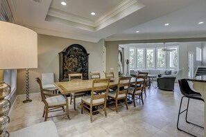 A dining area with a wooden table and chairs, a large decorative piece on the wall, and a view of a balcony with a sofa.